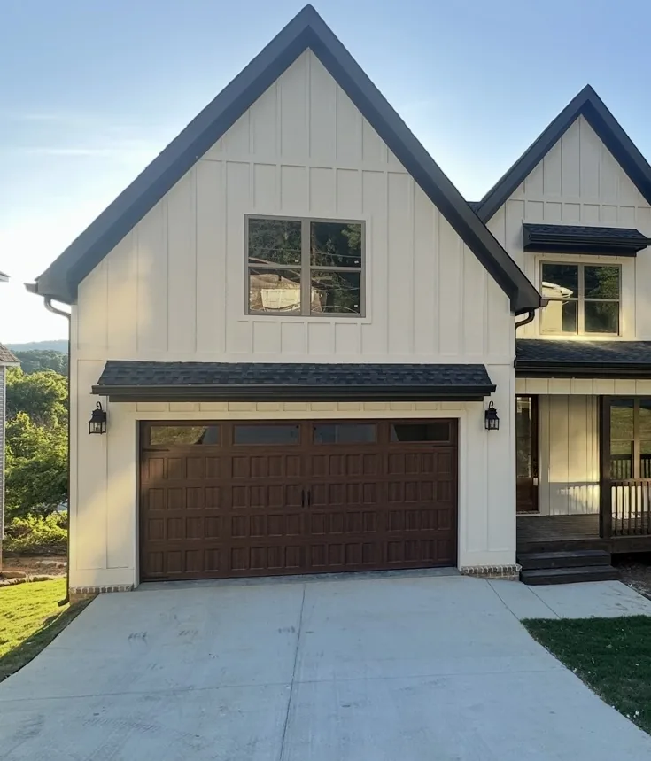 Wood-look residential garage door on a white board and batten home