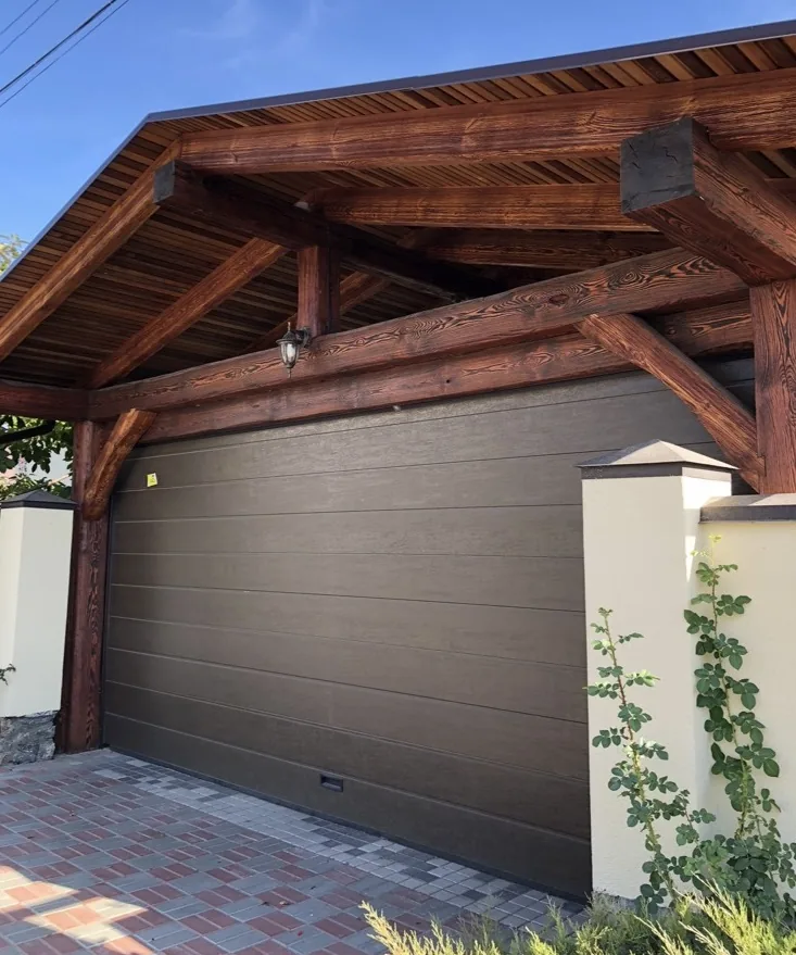 Modern brown residential garage door under a timber-framed carport