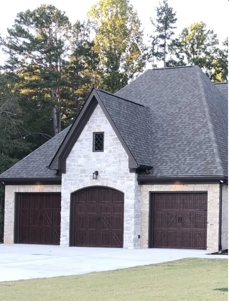 Three dark wood carriage style garage doors on a stone home