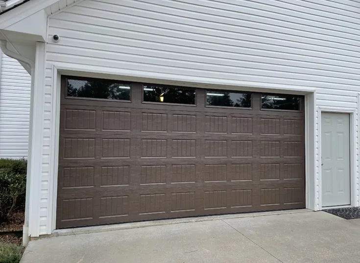 Brown residential garage door with upper windows on white siding